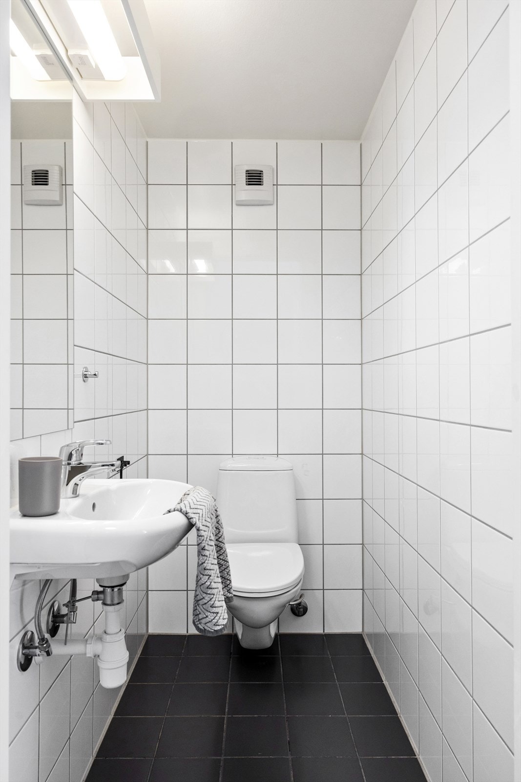 Praktisk, flislagt toalettrom bestående av servant og speil med lys over. Rommet har elektrisk avtrekk. Galleribilde