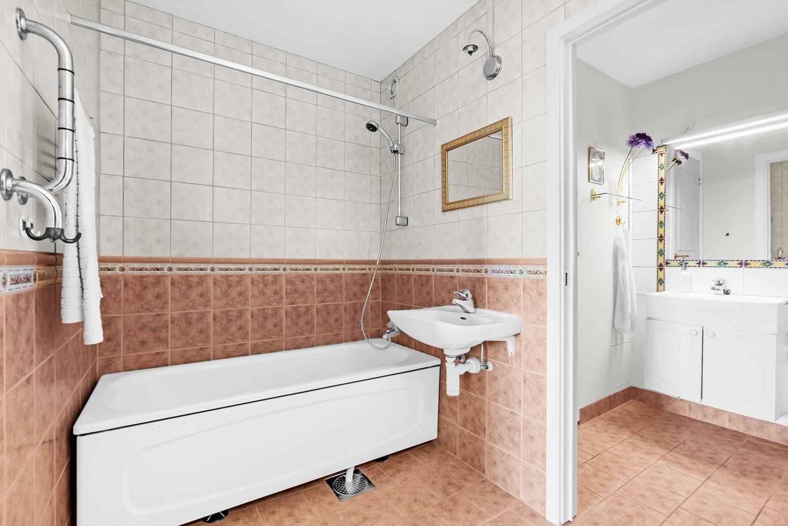 Baderomsdelen har servant og speil montert på vegg. Badekar med avløp direkte til sluk og dusjutstyr. Innredning med profilerte, folierte fronter og laminat benkeplate, speil og lysarmatur på vegg. Galleribilde