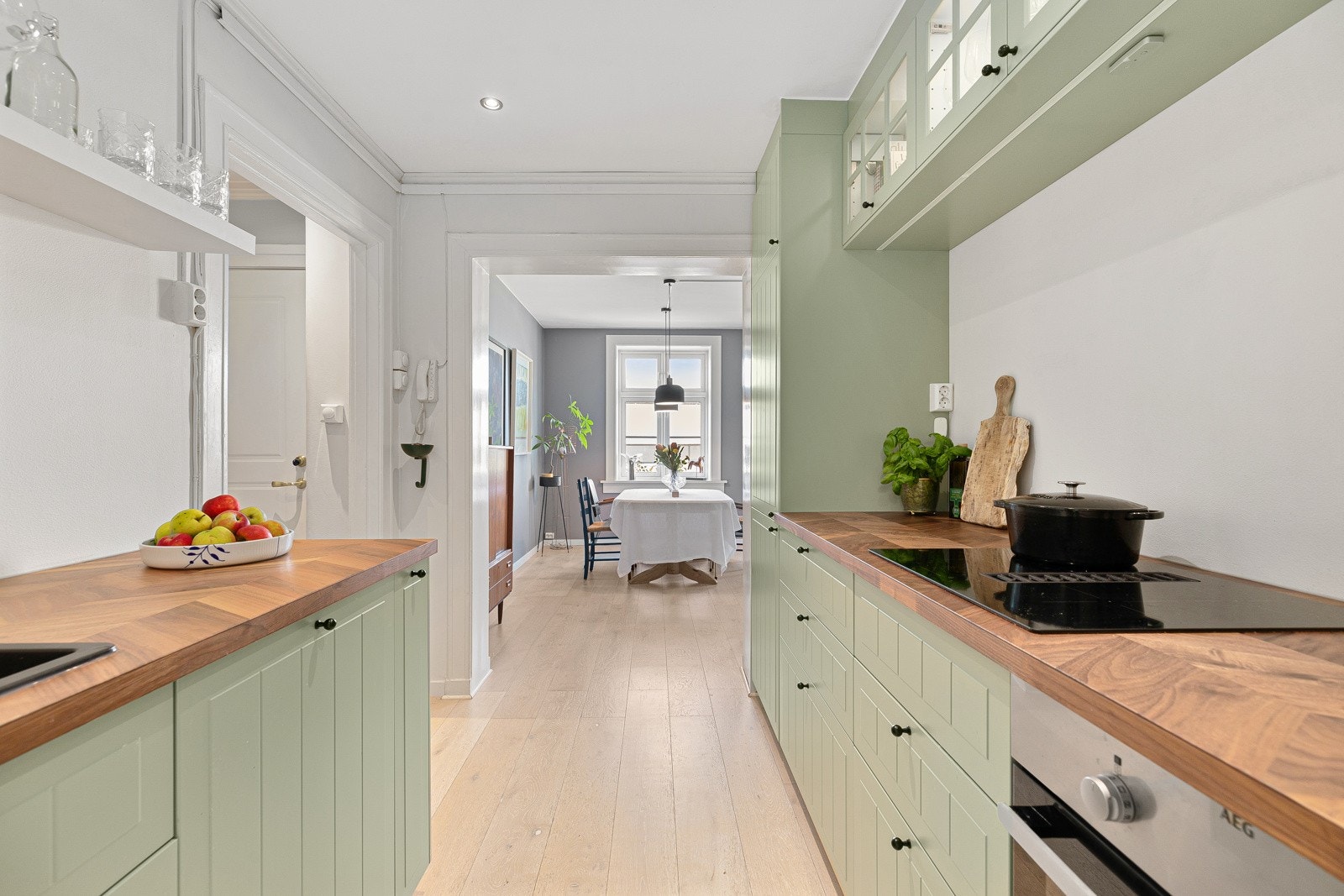 Lekkert kjøkken i en smakfull grønntone mot en lys benkeplate med nedfelt komposittvask og ett-greps armatur i sort Galleribilde