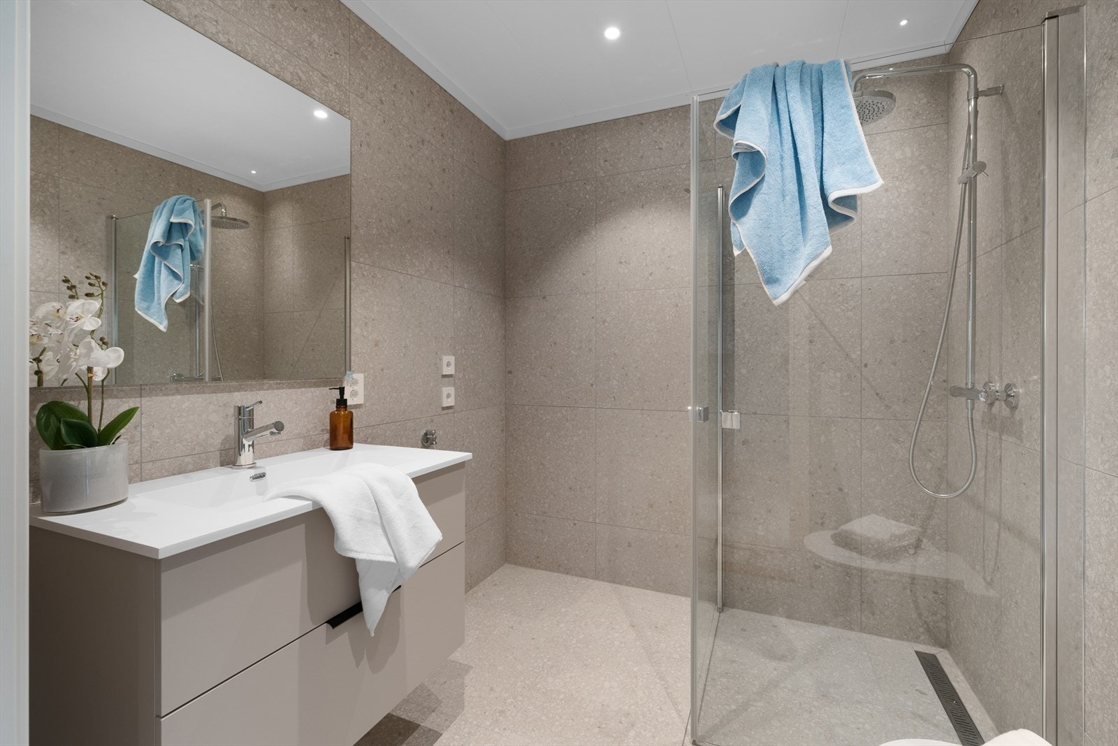 Boligen har også et bad i begge etasjene. Badene består av 60x60 flislagte vegger og gulv med varmekabler. Flisene er av type Match Up Suger mix. Himling i tak-ess. Komplette baderomsmøbler fra Aubo som er levert i samme overflater som kjøkken. Galleribilde