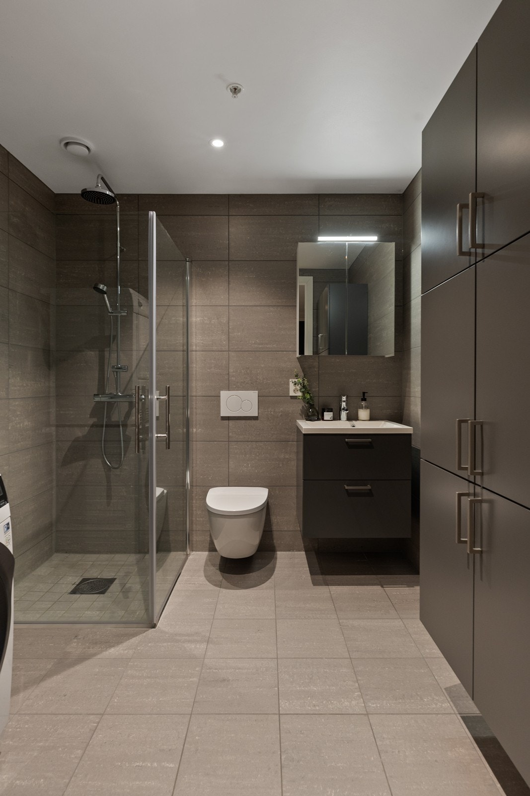 Baderommet er utstyrt med vegghengt WC, servant, dusjhjørne og opplegg for vaskemaskin. Det er skapinnredning med malte slette fronter på underskap og høyskap, og fronter med speil på overskap Galleribilde