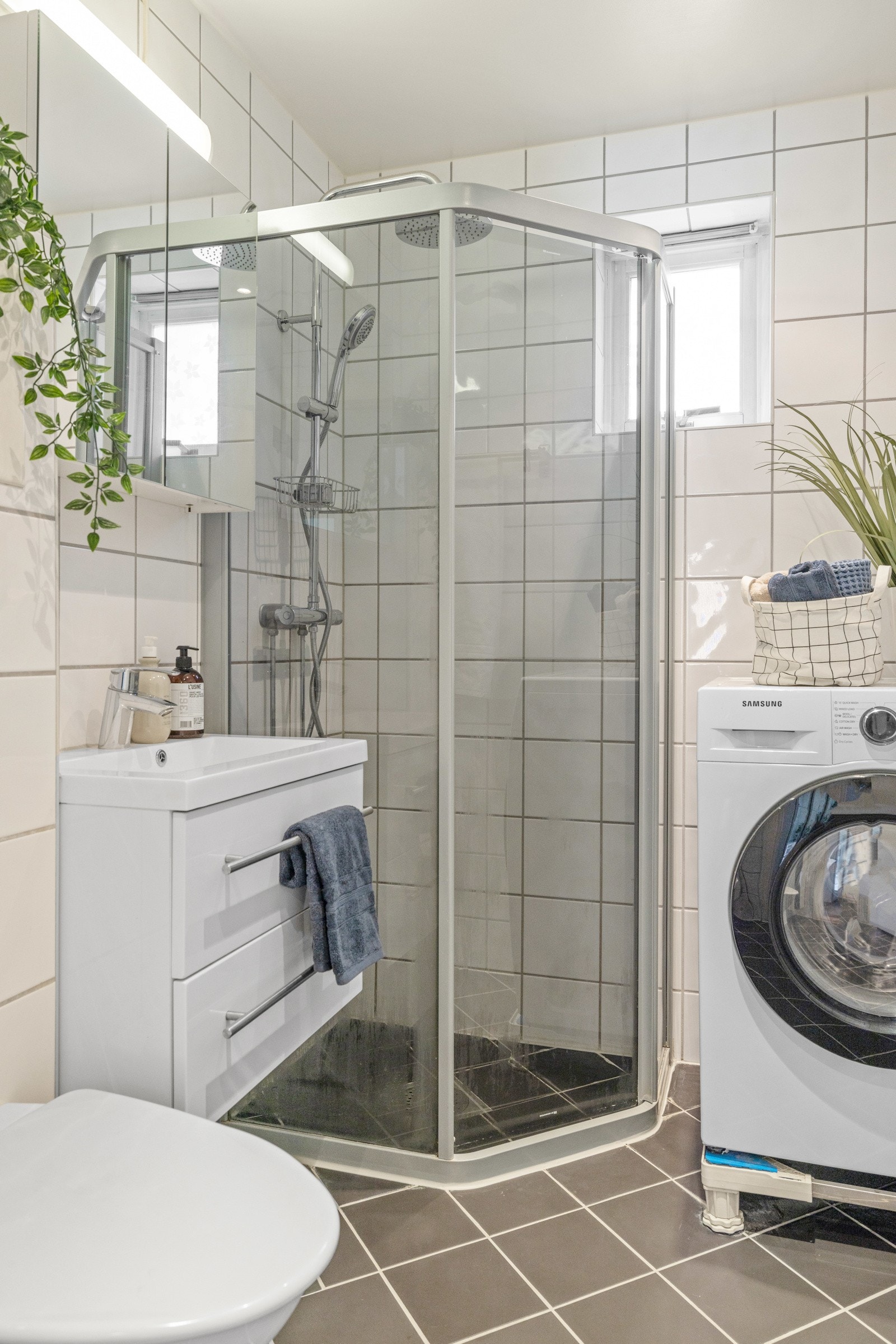 Badet har et vegghengt toalett, opplegg for vaskemaskin og et dusjhjørne med regnfallsdusj Galleribilde