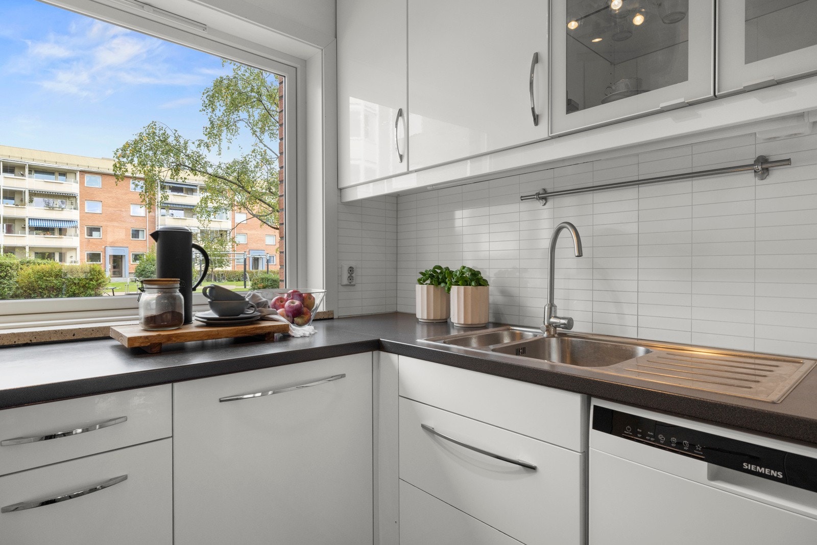 Innredningen har hvite høyglansfronter, takhøye skap og grå laminatbenkeplate med nedfelt kum i stål Galleribilde