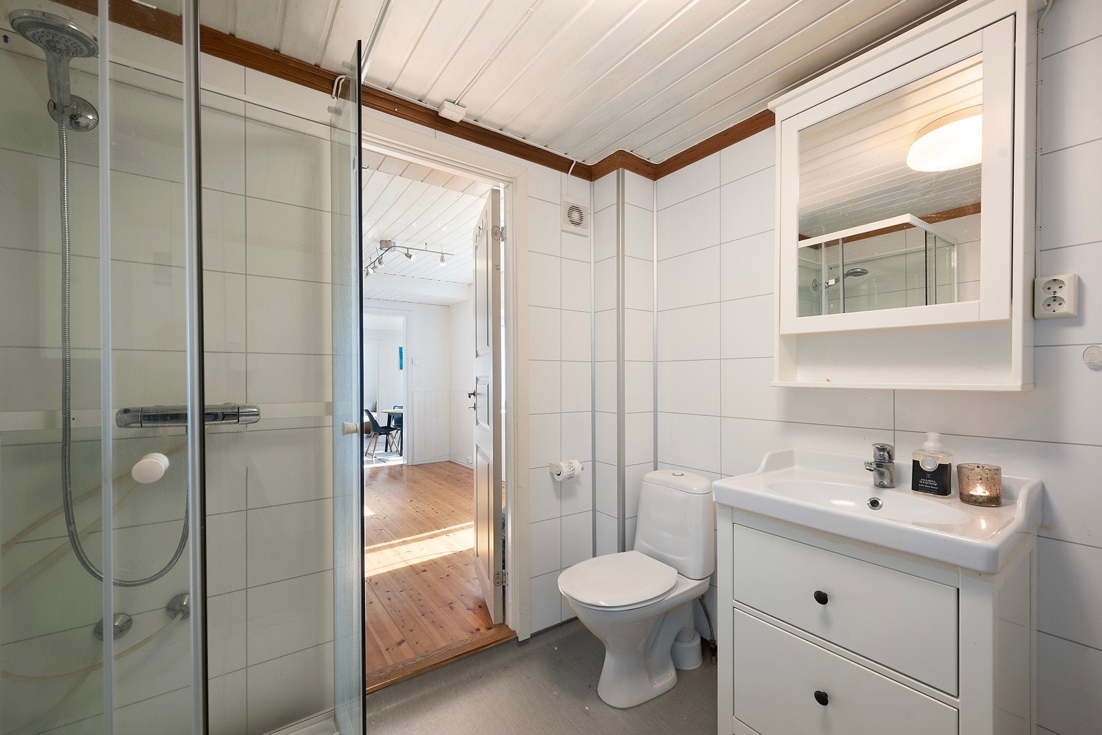 Fra kjøkkenet er det inngang til boligens bad med vinylbelagt gulv og baderomspanel på veggene. Badet inneholder dusjkabinett, servantinnredning og toalett Galleribilde