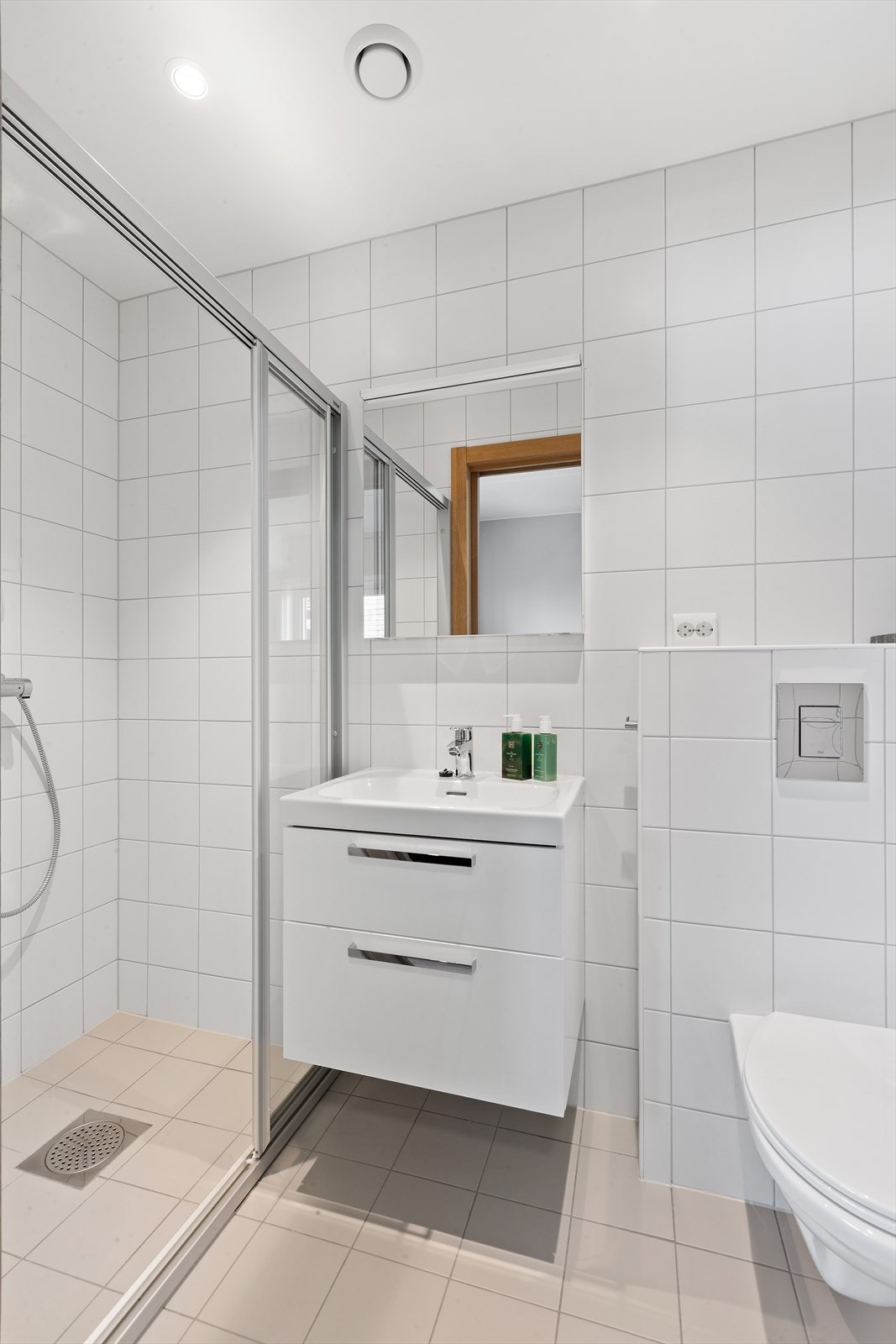 Videre er badet utstyrt med dusjhjørne, en moderne servantinnredning og vegghengt toalett. Galleribilde