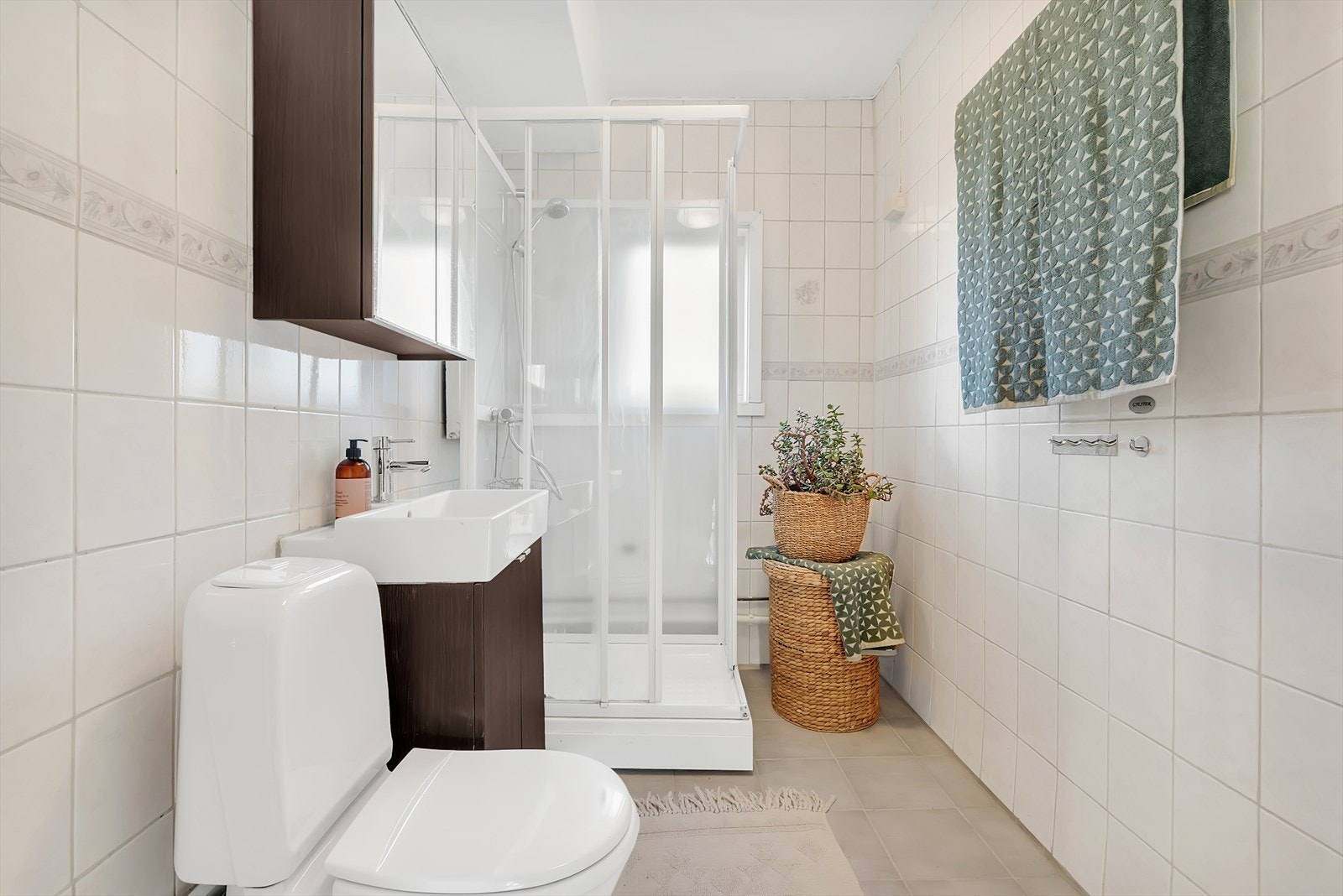 Bad med fliser på gulv, malt mdf plater på en vegg samt fliser, malt tak. Innredningen består av wc, servant med underskap, overskap med speildører og dusjkabinett. Galleribilde