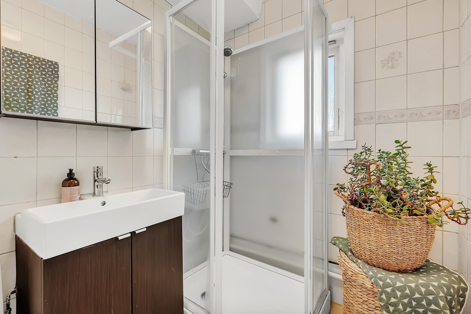 Bad med fliser på gulv, malt mdf plater på en vegg samt fliser, malt tak. Innredningen består av wc, servant med underskap, overskap med speildører og dusjkabinett. Galleribilde