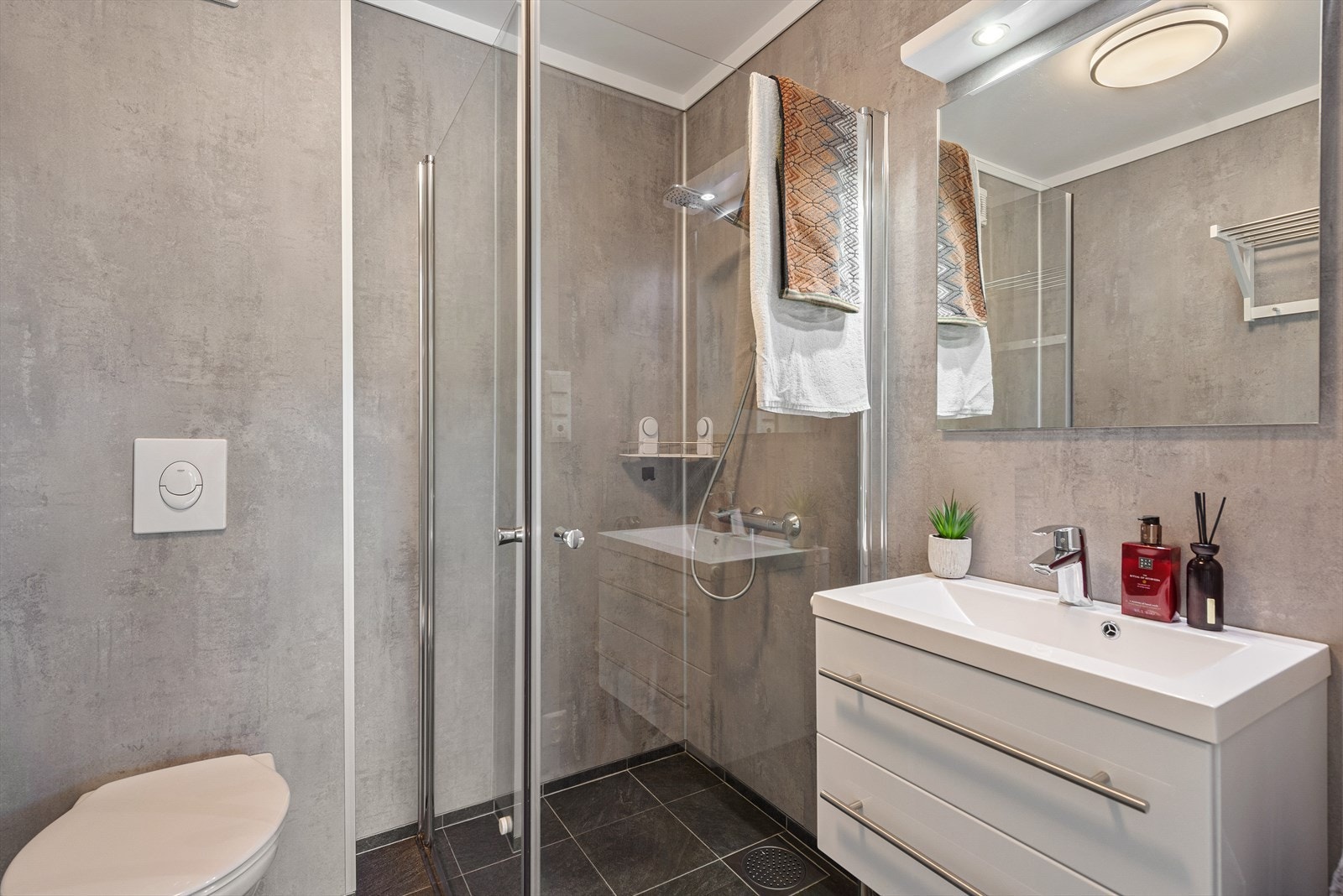 Flislagt gulv i baderom med gulvvarme og baderomsplater på vegger. Malt himling. Innredet med servantskap, vegghengt toalett og dusj med glassdører. Galleribilde