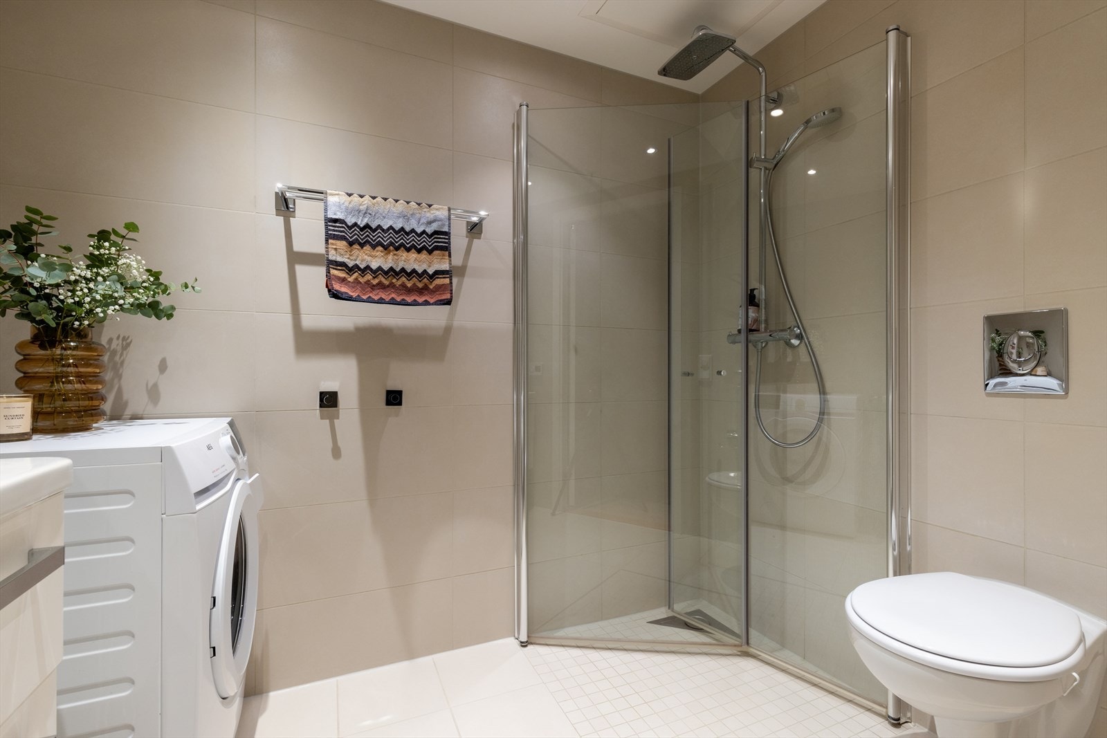 Badet inneholder dusjnisje med innfelbare glassvegger, servant med skuffer, speilskap, vegghengt toalett og opplegg for vaskemaskin. Galleribilde