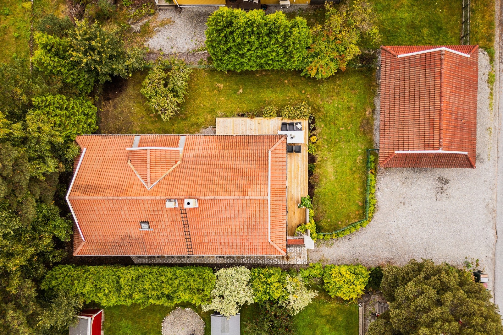 Gårdsplassen er gruset og har plass til flere biler. Tomten er frodig og grønn med et vell av trær, busker og hekk som gir skjerming langs tomtegrensen. Galleribilde