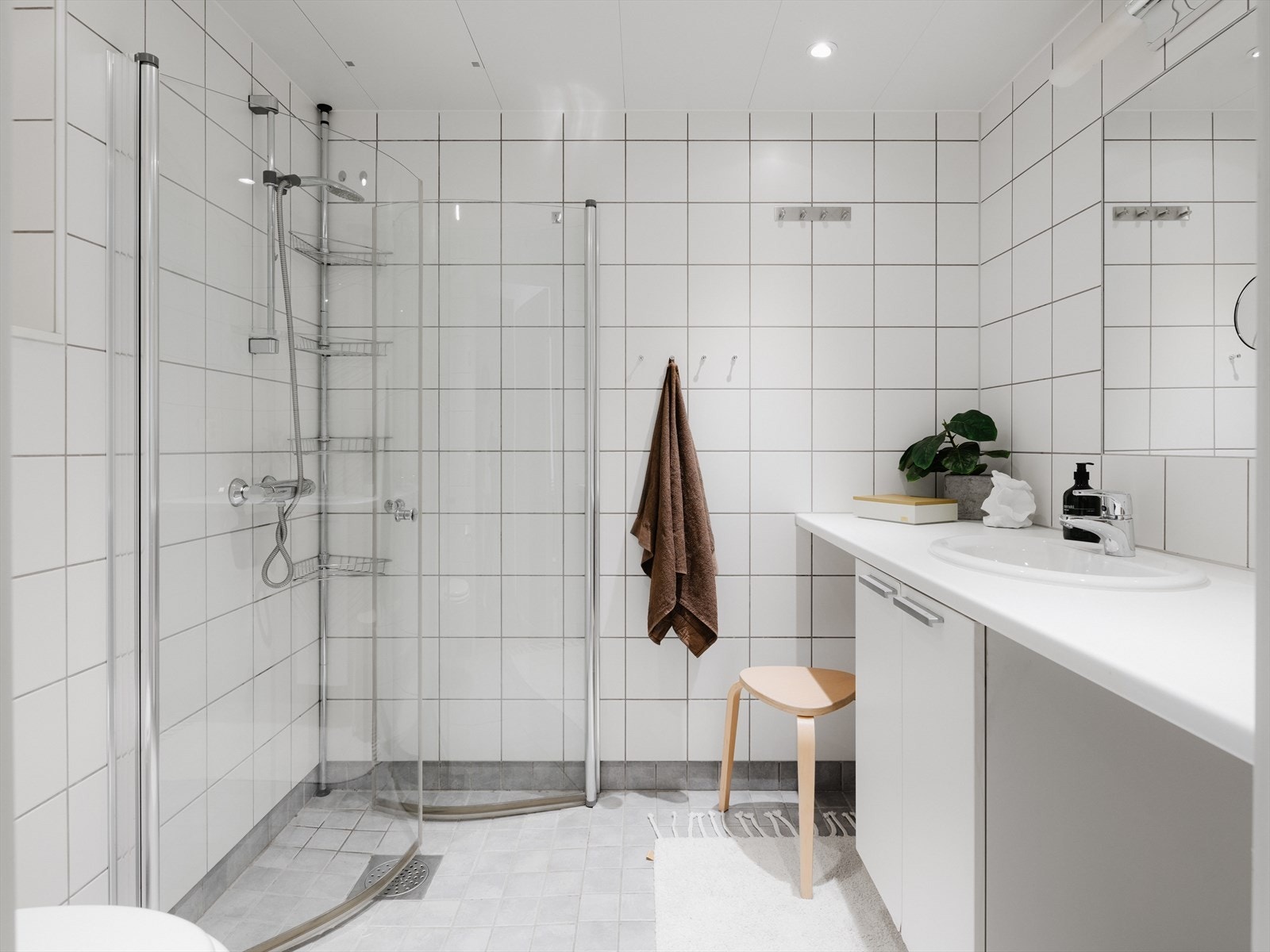 Lyst, flislagt bad i en tidsnøytral utførelse. Praktiske innfellbare dusjdører og avsatt plass til både vaskemaskin og tørketrommel. Galleribilde