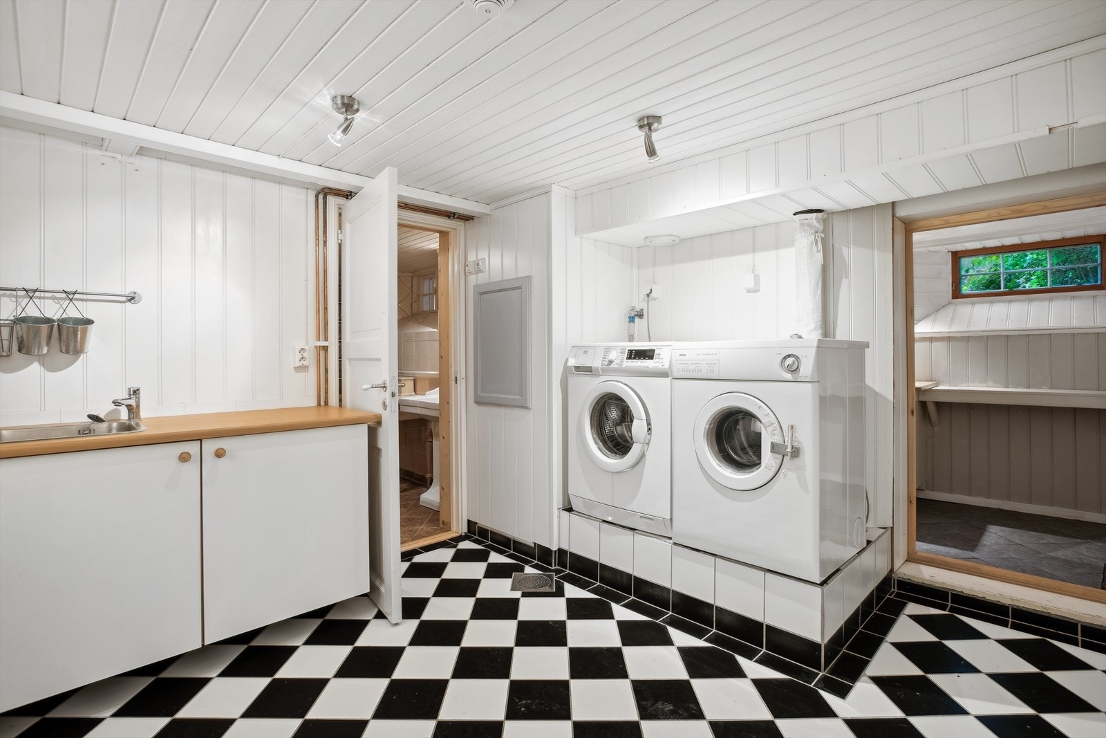 Praktisk vaskerom med fliser på gulv og mdf på vegger. Servant og opplegg for vaskemaskin. Hvit glatt innredning med laminert benkeplate. Galleribilde
