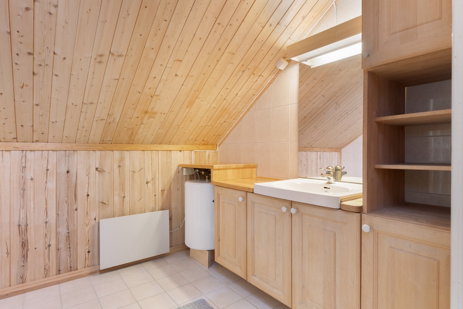 Badet i loftetasjen innehar standard fra 1986. Her er det romslig baderomsinnredning med skap, åpne hyller og benkeplate med nedfelt servant. Galleribilde