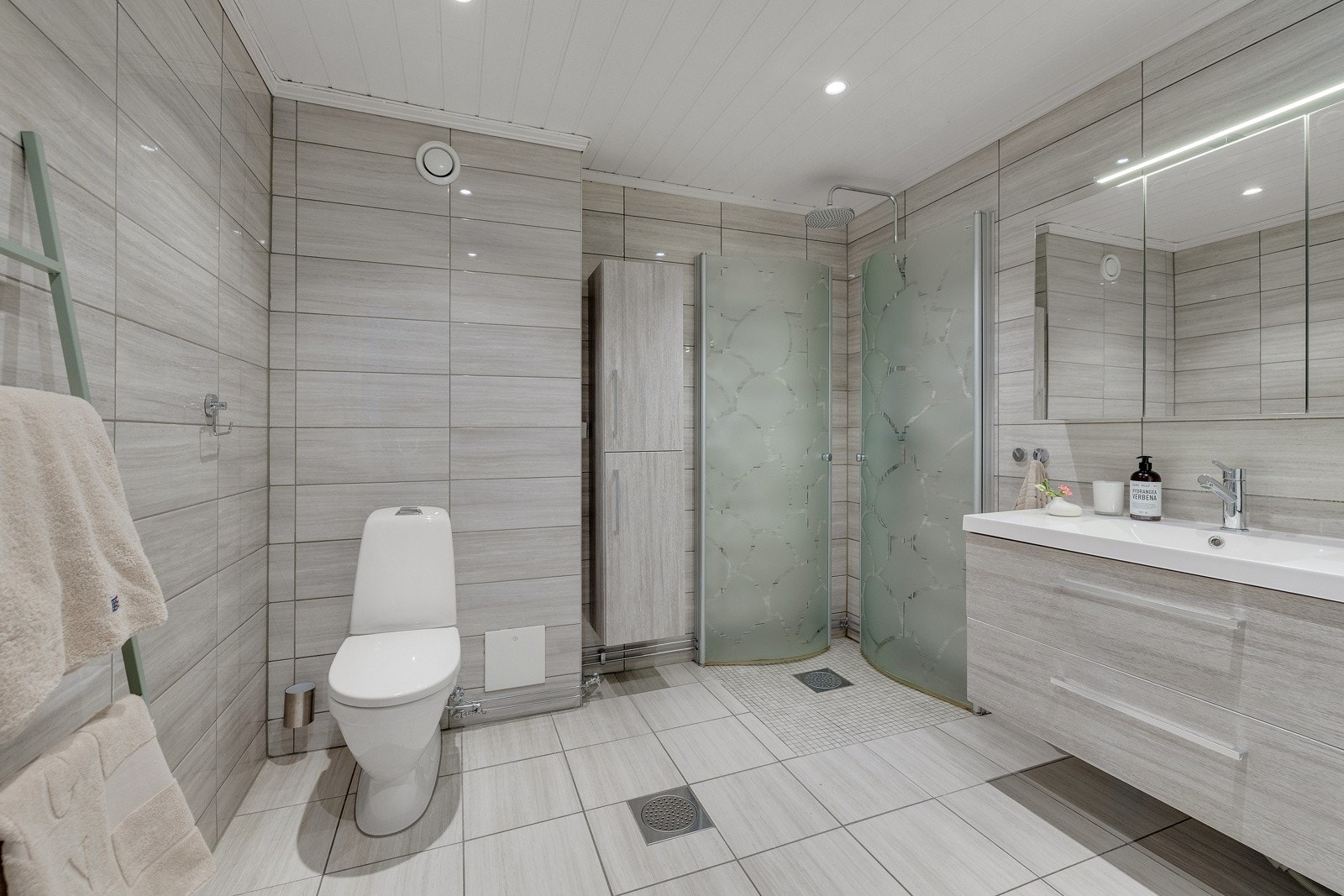 Badet har moderne innredning med servant på vegghengt servantskap, gulvstående toalett, samt dusjhjørne med vegghengte dusjdører i glass. Galleribilde