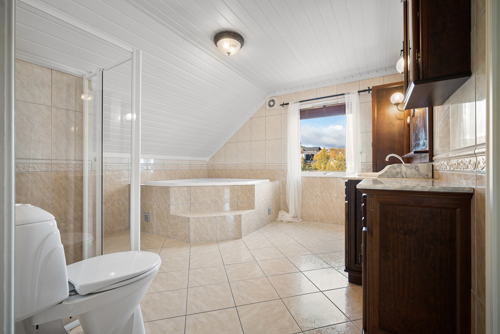 Badet inneholder innebygd hjørnebadekar, dusjkabinett, toalett og servantinnredning med god plass for toalettsaker og håndklær Galleribilde