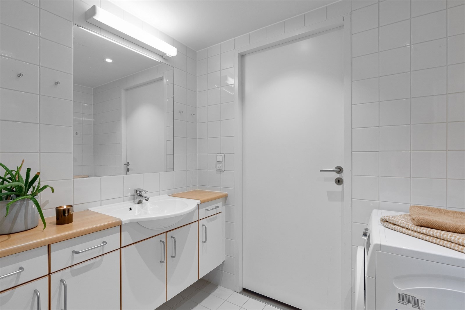 Baderomsinnredning med hvite glatte fronter og laminert benkeplate og med nedfelt porselenservant, innfliset speil og lysarmatur Galleribilde