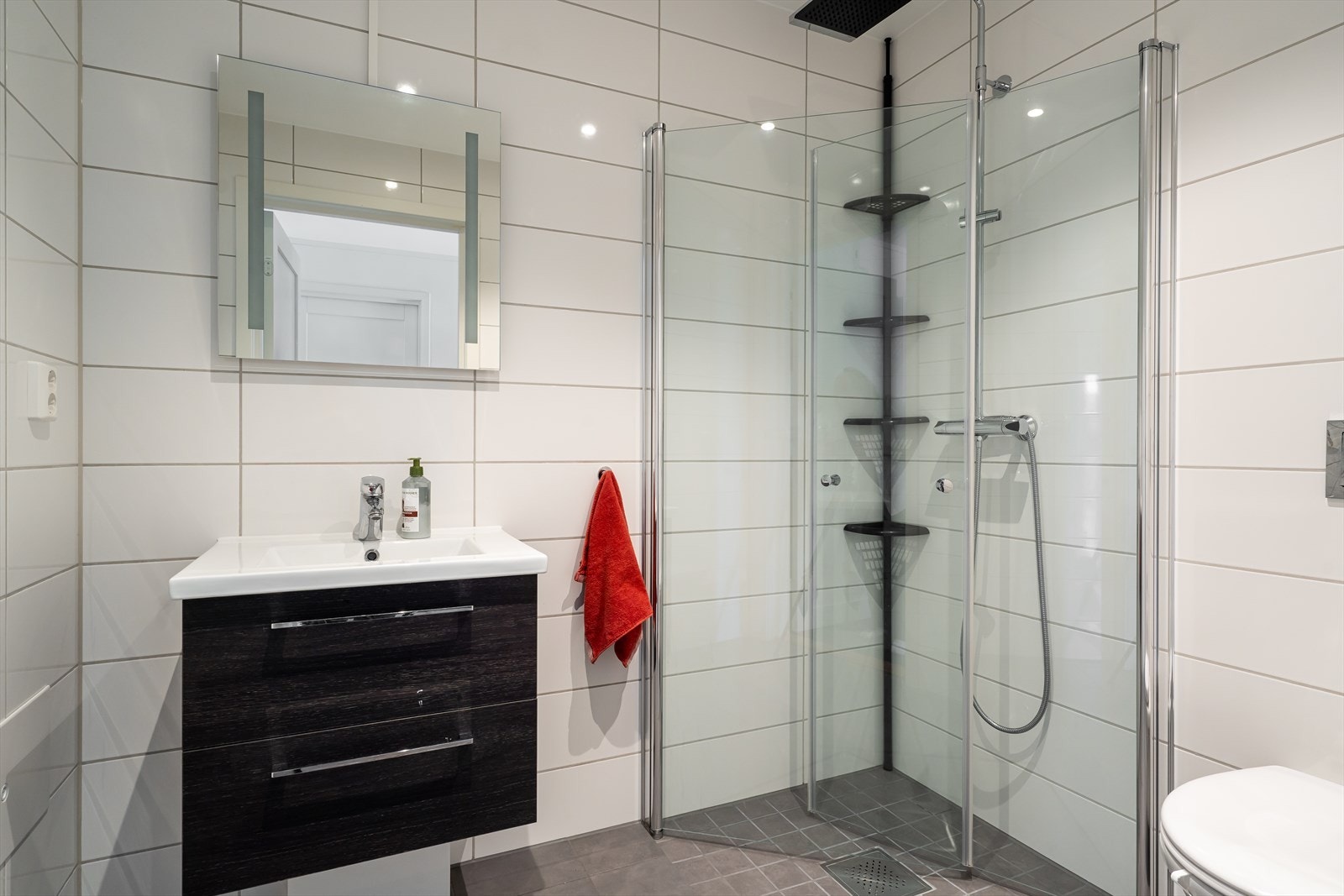 Badet i førsteetasje består av dusjhjørne med innfeldbare glassdører, vegghengt toalett, sort innredning og vegghengt speil med lys. Galleribilde