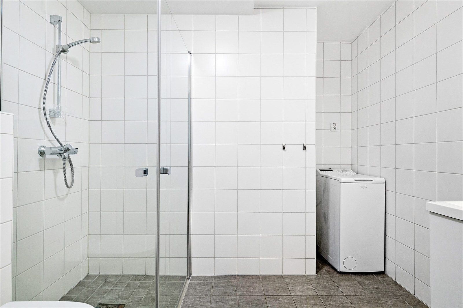 Badet er innredet med baderomsinnredning, vegghengt toalett, dusjhjørne og opplegg for vaskemaskin. Galleribilde