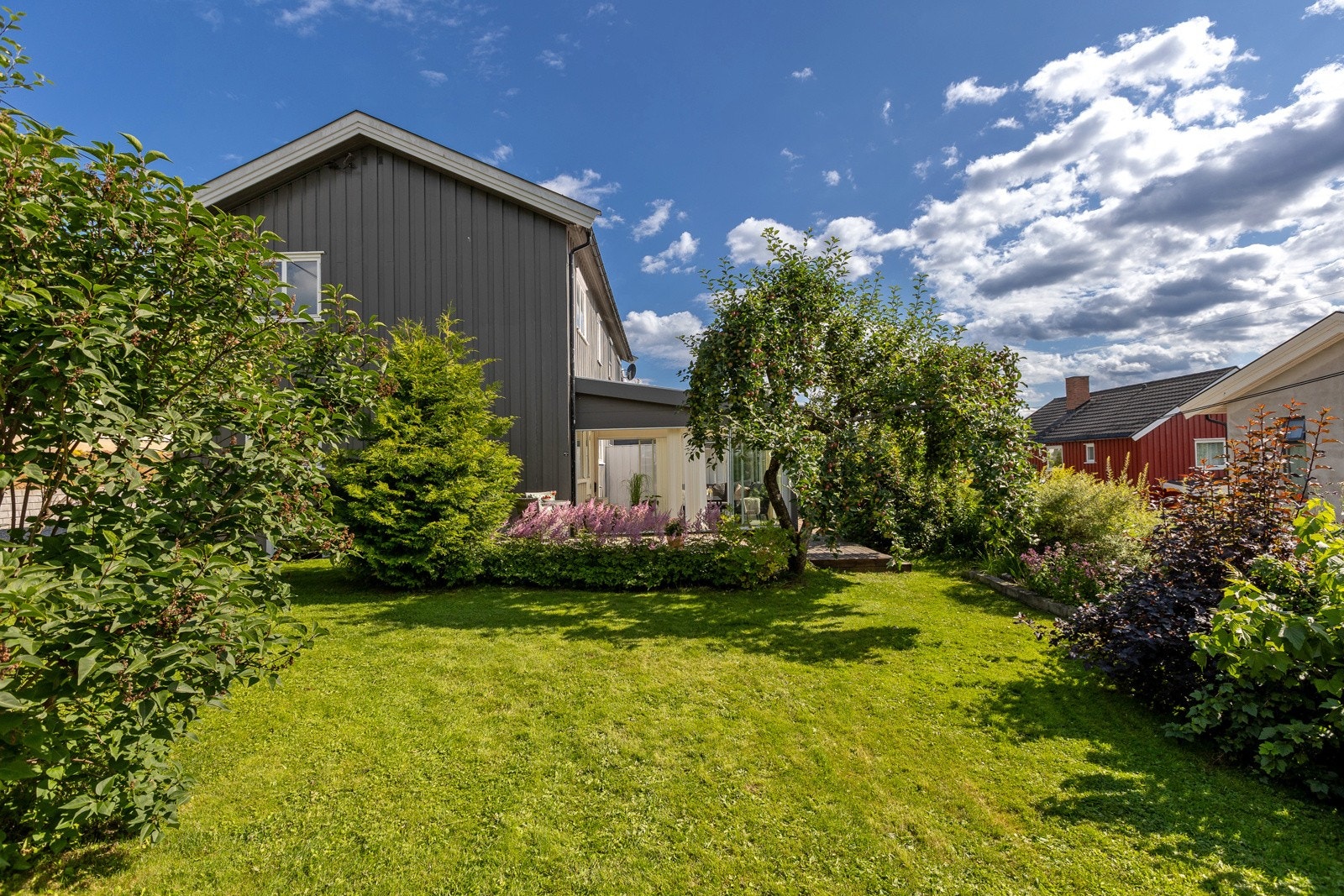 Velstelt og frodig hage bestående av plenarealer og beplantninger. Galleribilde