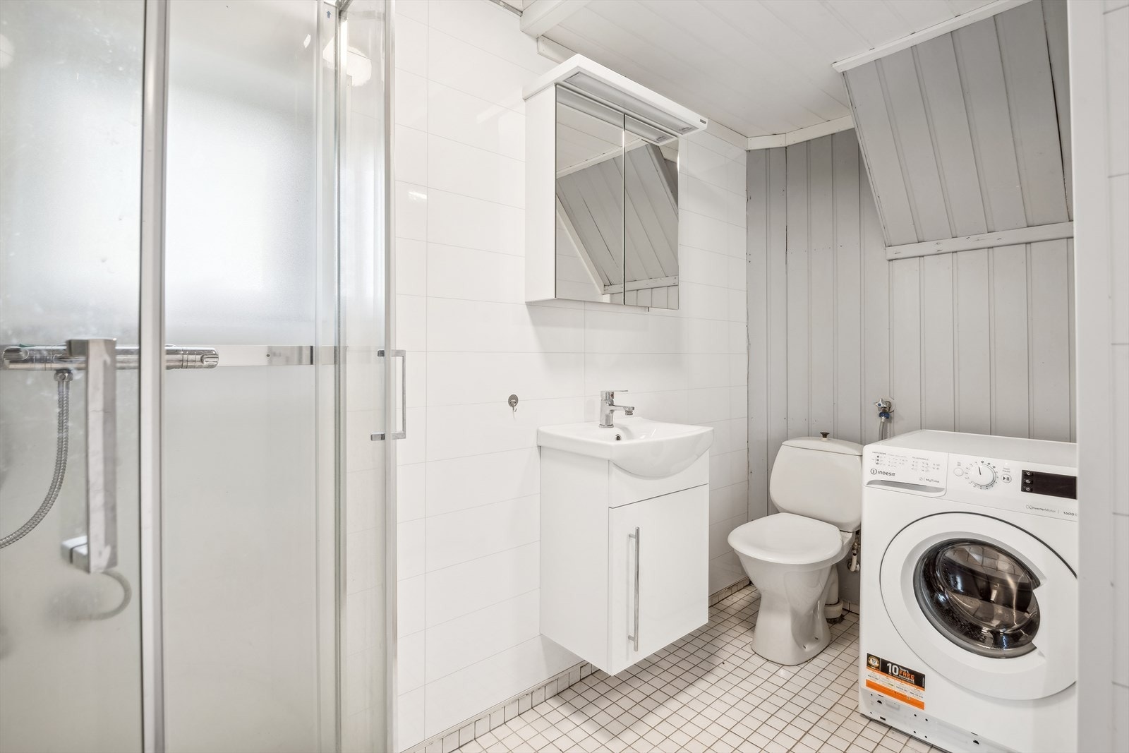 Bad kjeller har baderomsplater på veggene og fliser på gulvet. Badet har baderomsinnredning, toalett og dusjkabinett. Galleribilde