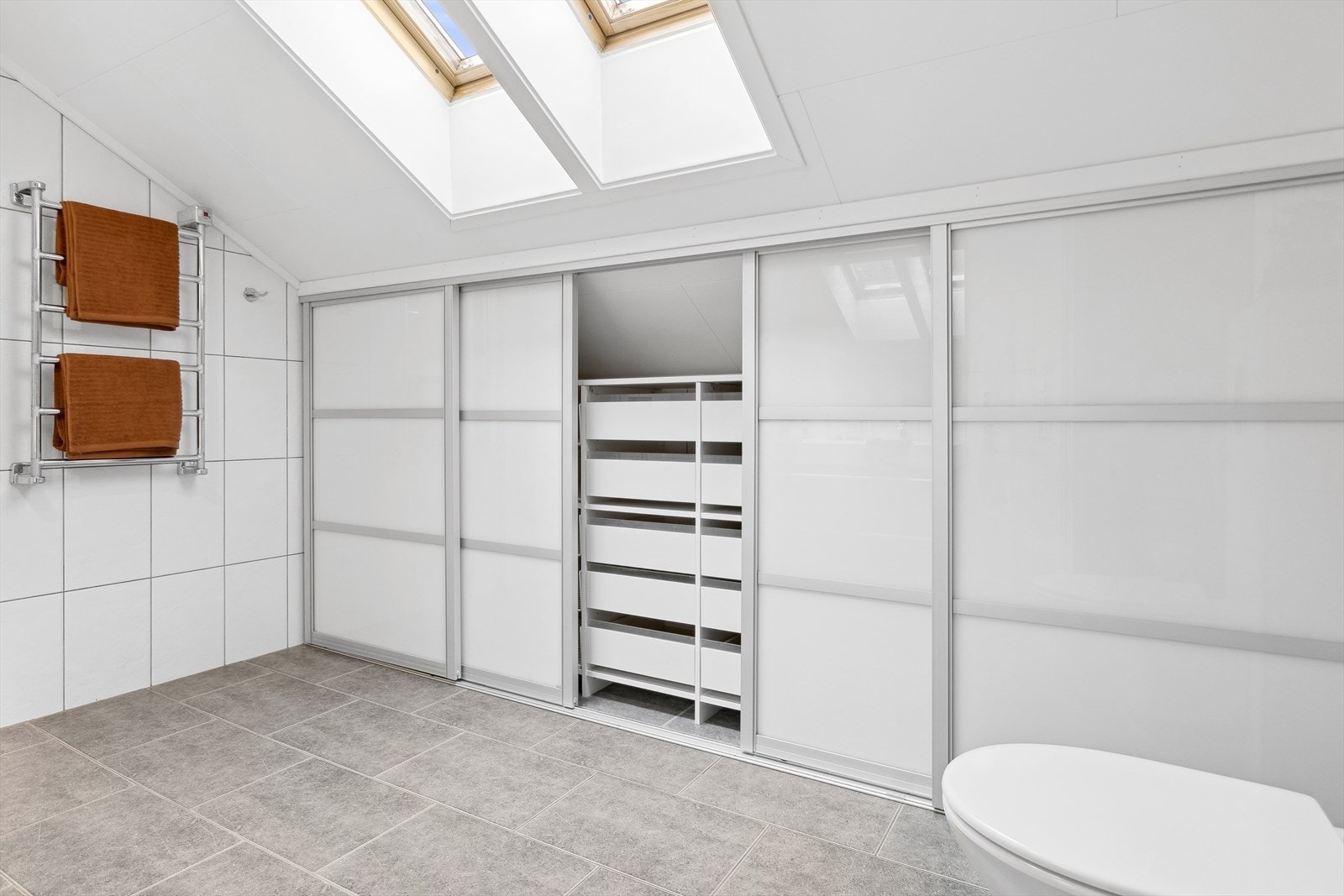 Det er tilpasset skyvedørsgarderobe langs hele langveggen der håndklær og andre baderomsartikler enkelt kan gjemmes bort Galleribilde
