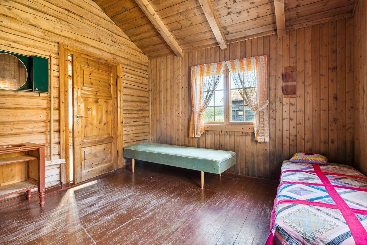 Ett soverom i gammelstuen. Dette rommet har malt tregulv og tømmer og trepanel på veggene. Rommet er romslig med flere vinduer som slipper inn dagslyset. Galleribilde