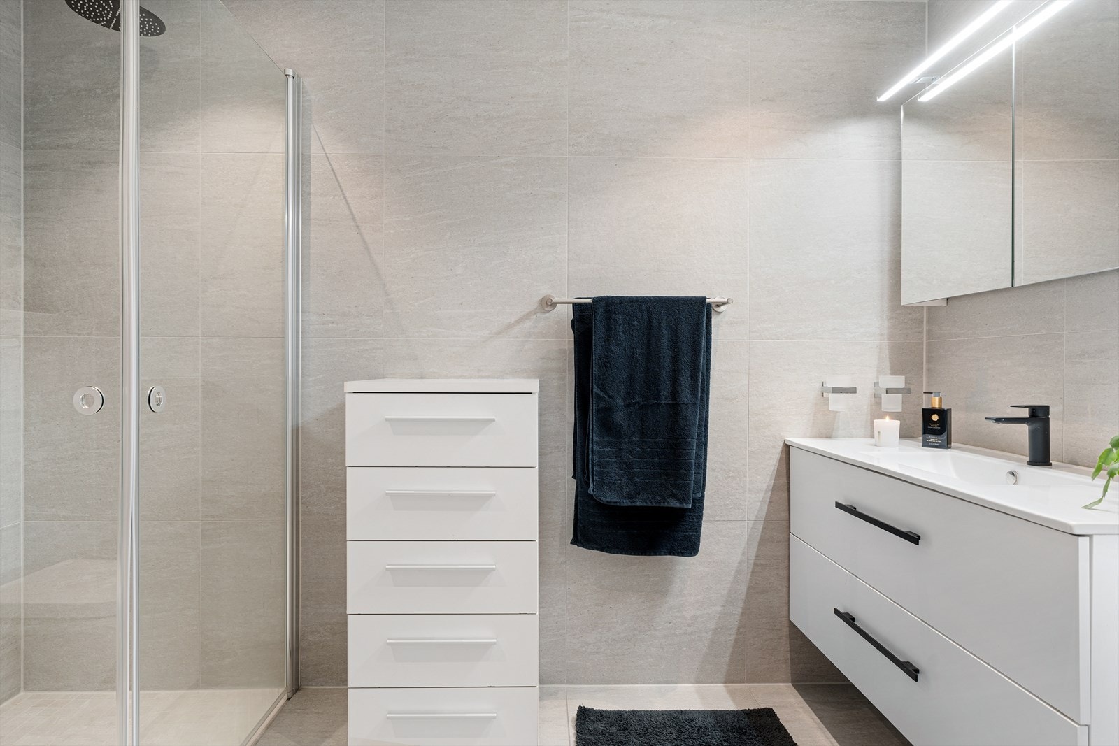 Badet inneholder dusjhjørne med regndusj, innredning med servant, speilskap og vegghengt toalett. Galleribilde