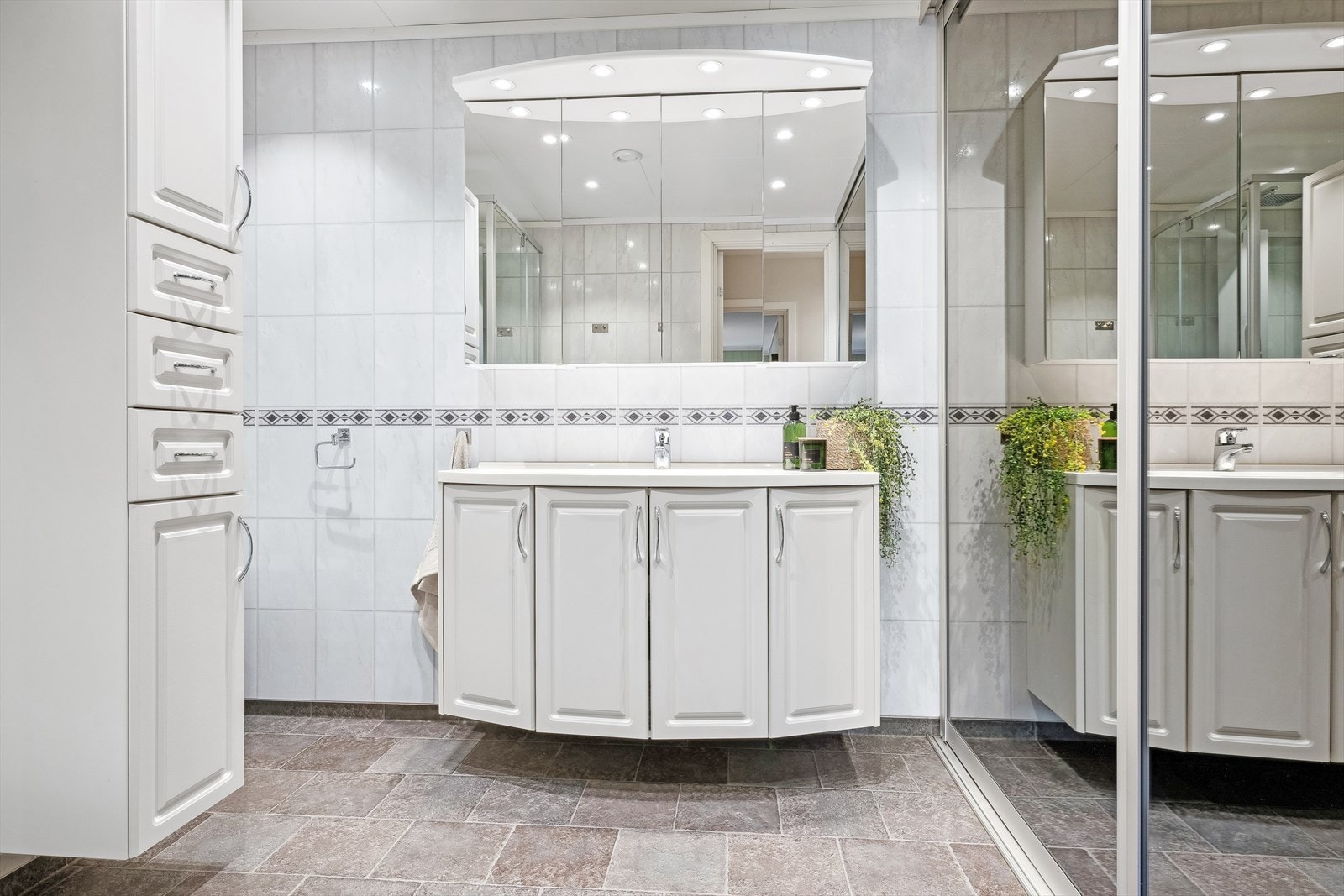 Baderom utstyrt med heldekkende servant på skapinnredning, samt overskap med speildører og belysning Galleribilde