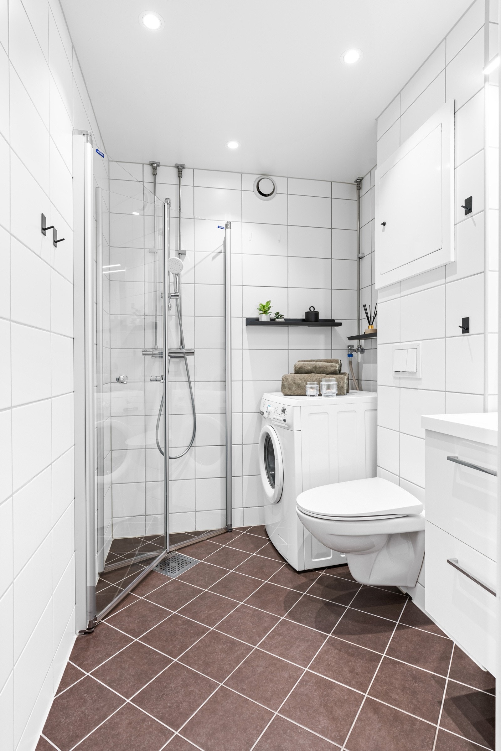 Veggmontert toalett, og et dusjhjørne med innfellbare glassdører. I hjørnet av rommet er det montert opplegg for vaskemaskin. Galleribilde