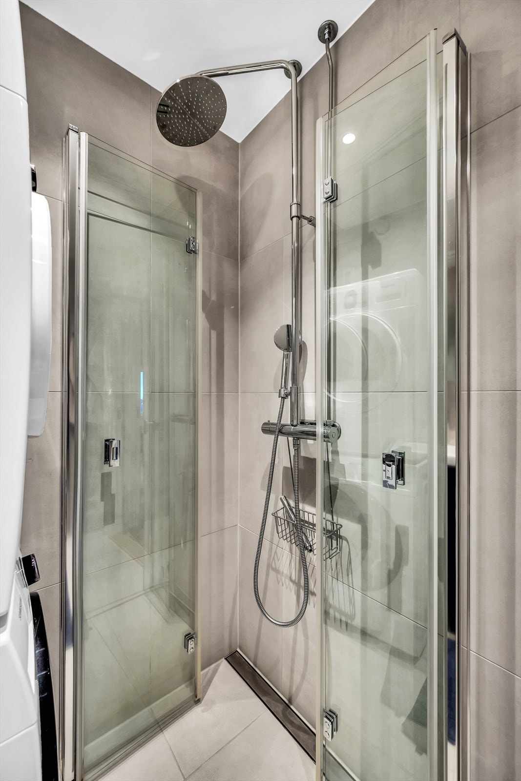 Badet er utstyrt med veggmontert toalett, dusjhjørne med innfellbare dusjdører og baderomsinnredning med skuffer, servant og speilskap. Galleribilde