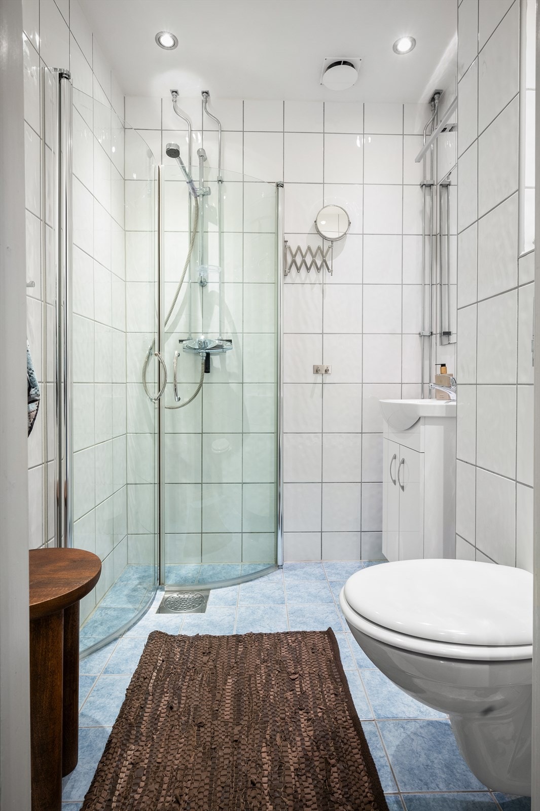 Baderomsinnredning bestående av benkeskap og veggskap med glatte fronter. Speil og belysning over servant. Dusj på gulv, servant i helstøpt plate, veggfestet klosett med innebygget sisterne og opplegg for vaskemaskin. Galleribilde