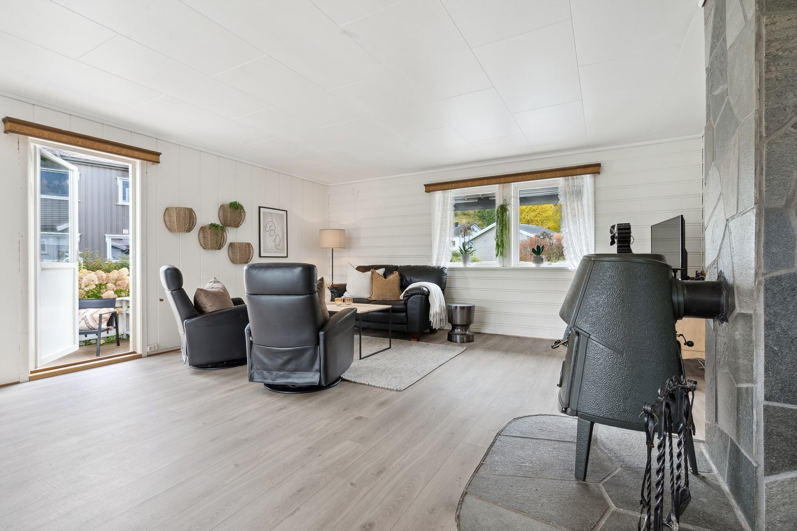 Stuen har vedovn montert foran en steinkledd brannvegg, noe som bidrar til rommets trivelige atmosfære. Galleribilde