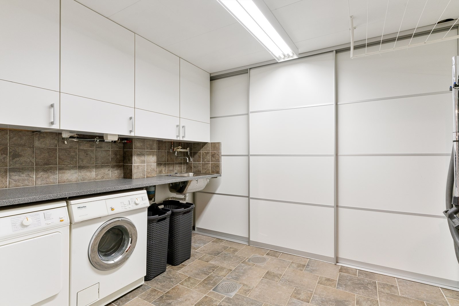 Romslig vaskerom med skyvdørsgardobe, innredning, utslagsvask og opplegg for vaskemaskin/tørketrommel. Galleribilde