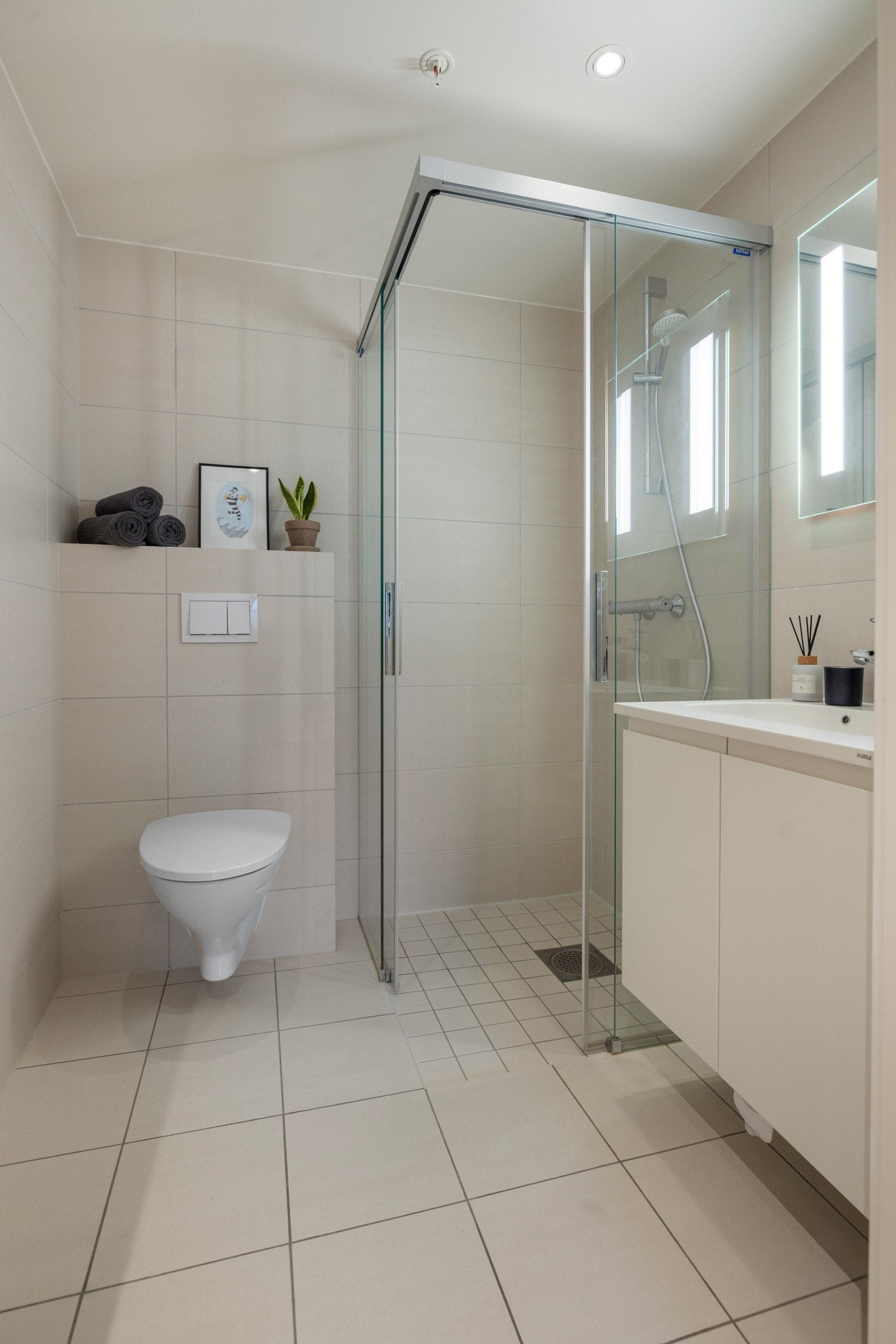 Det andre badet har dusj med glassvegger, et vegghengt toalett, speil med belysning og servant med underskap Galleribilde