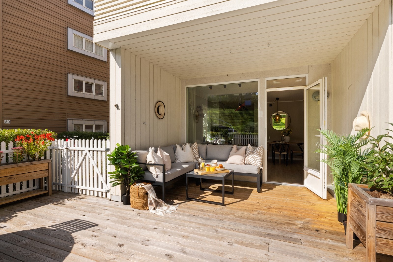 Gulvet er lagt med terrassebord og rundt er det et koselig, hvitmalt stakittgjerde med tette, grønne hekker på utsiden Galleribilde