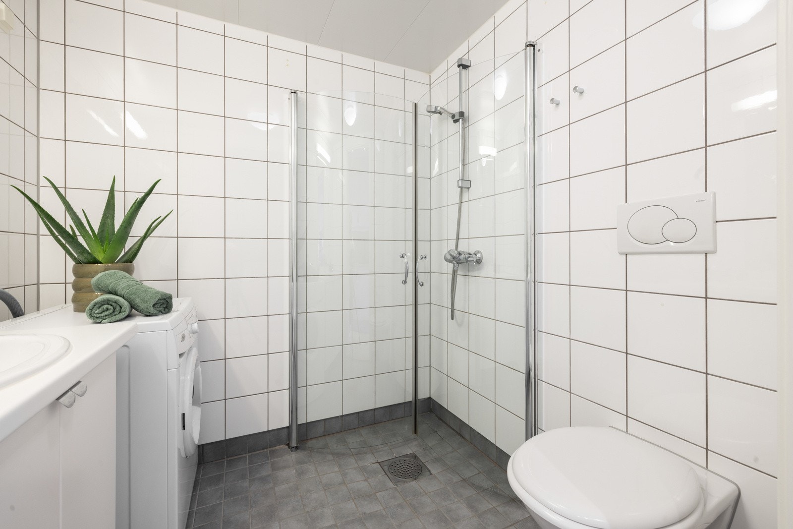 Badet er klassisk med hvite veggfliser og grå gulvfliser med gulvvarme Galleribilde