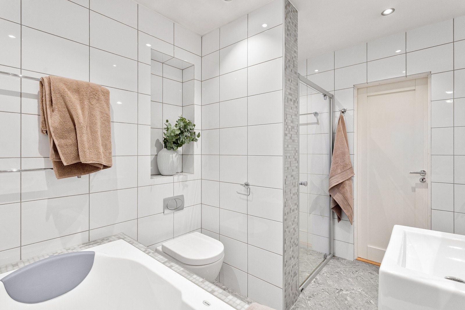 Baderommet har grå fliser på gulv med gulvvarme, hvite fliser på veggene og downlights i himlingen. Galleribilde