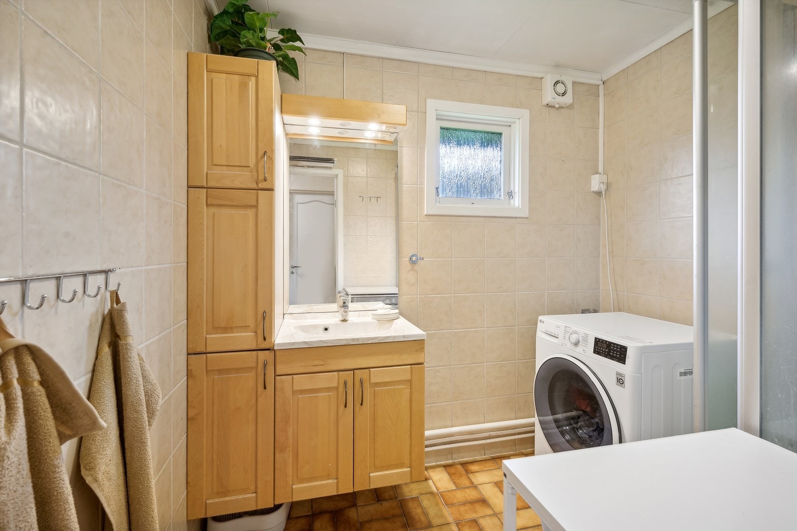 Flislagt bad med opplegg for vaskemaskin og god baderomsinnredning Galleribilde