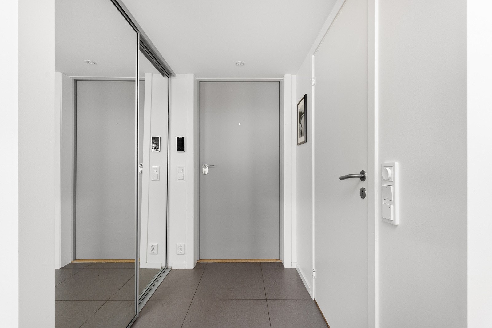 Entréen har store fliser på gulv med gulvvarme, glatte lysmalte overflater, skjult elektrisk anlegg og downlights i himlingen. Galleribilde