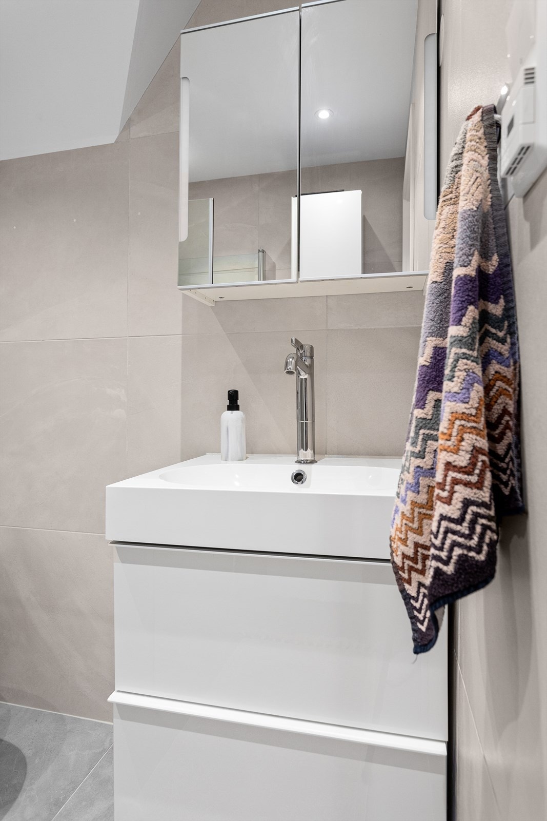 Baderom med vegghengt wc, servant med skuffer under, samt speilskap over og dusj i hjørne med innadslående dører. Galleribilde