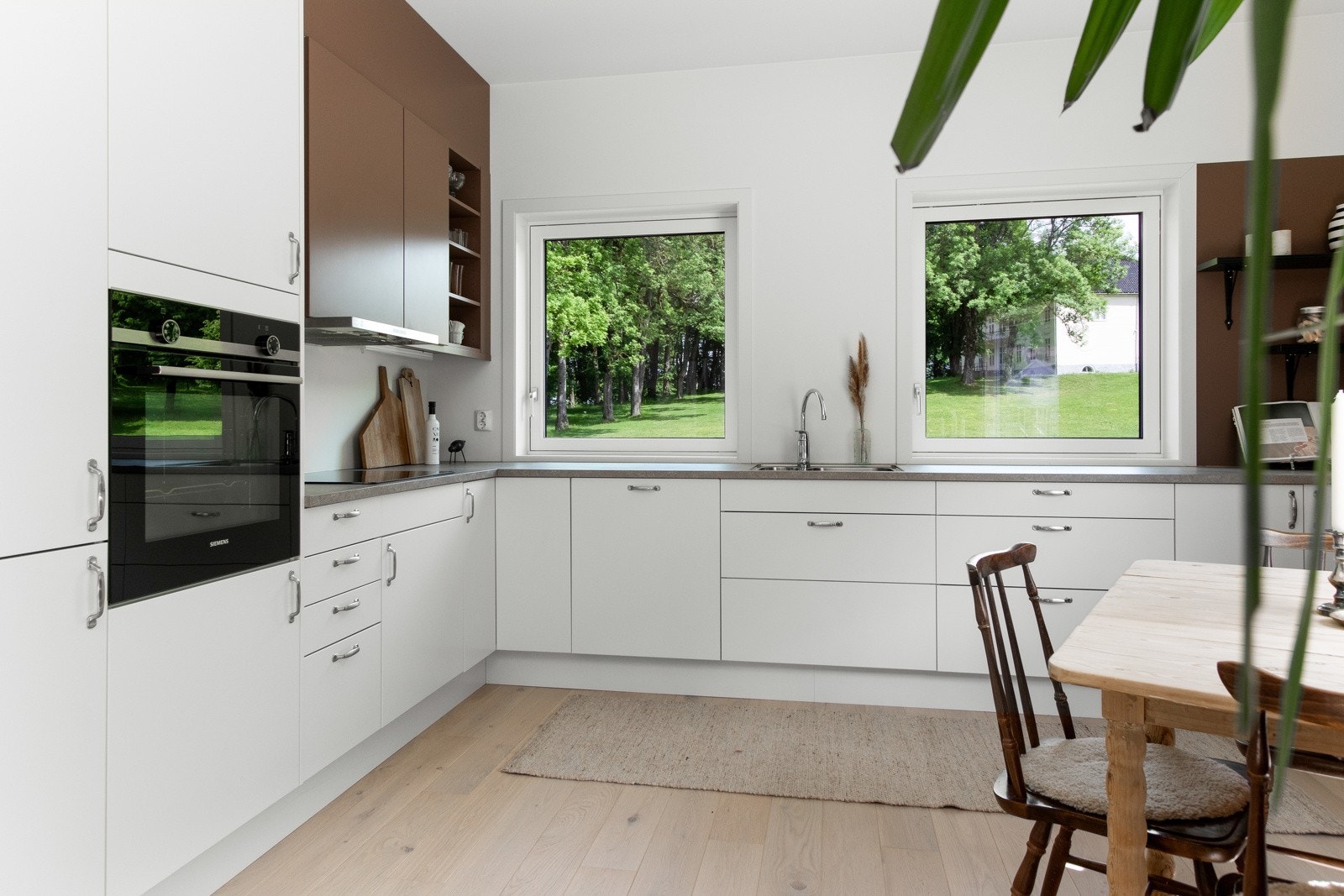 Innredningen har hvite, glatte fronter, overskap i en jordnyanse som matcher veggene og benkeplate av høytrykkslaminat med dobbel nedfelt oppvaskkum i rustfritt stål. Galleribilde