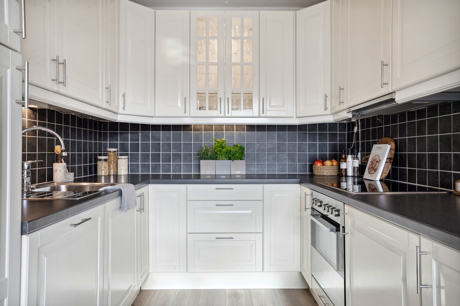 Benkeskapsbelysning og stikkontakter over kjøkkenbenk med integrert stekeovn, platetopp, oppvaskmaskin og kjøleskap. Galleribilde