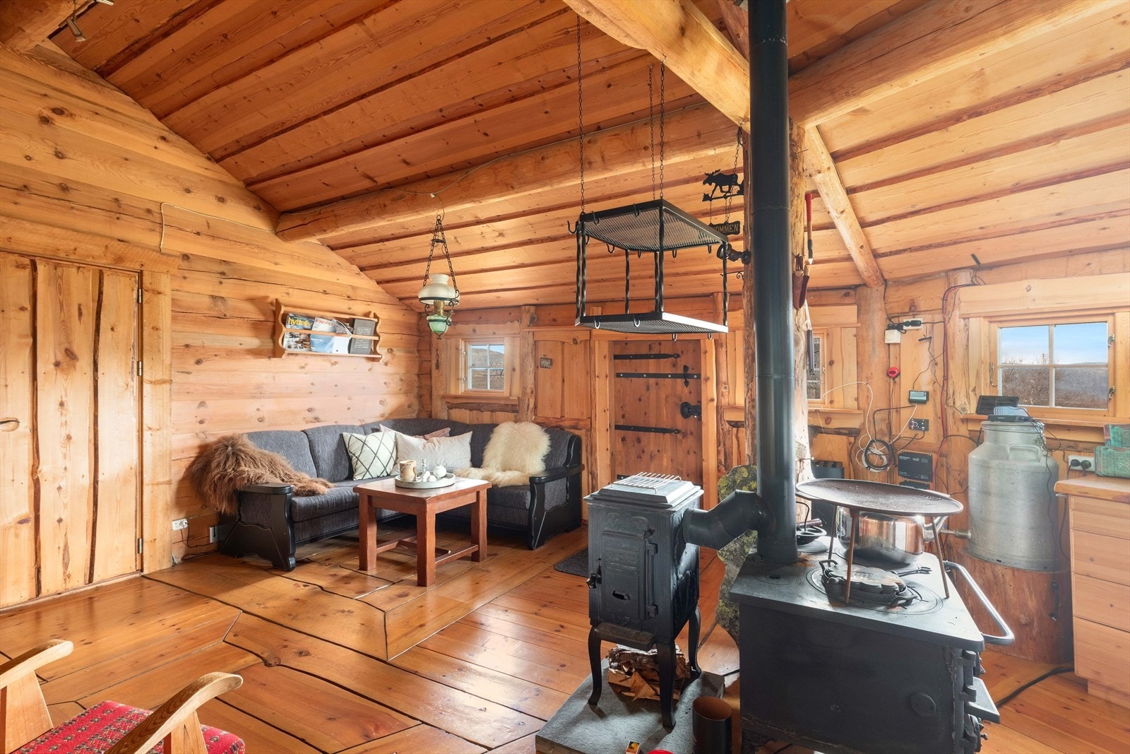 Vedovn og vedkomfyr sentralt i rommet. Døren til venstre går inn til soverom/stue hvor det er plassbygd køyeseng med dobbelseng nede og enkelseng oppe. Galleribilde