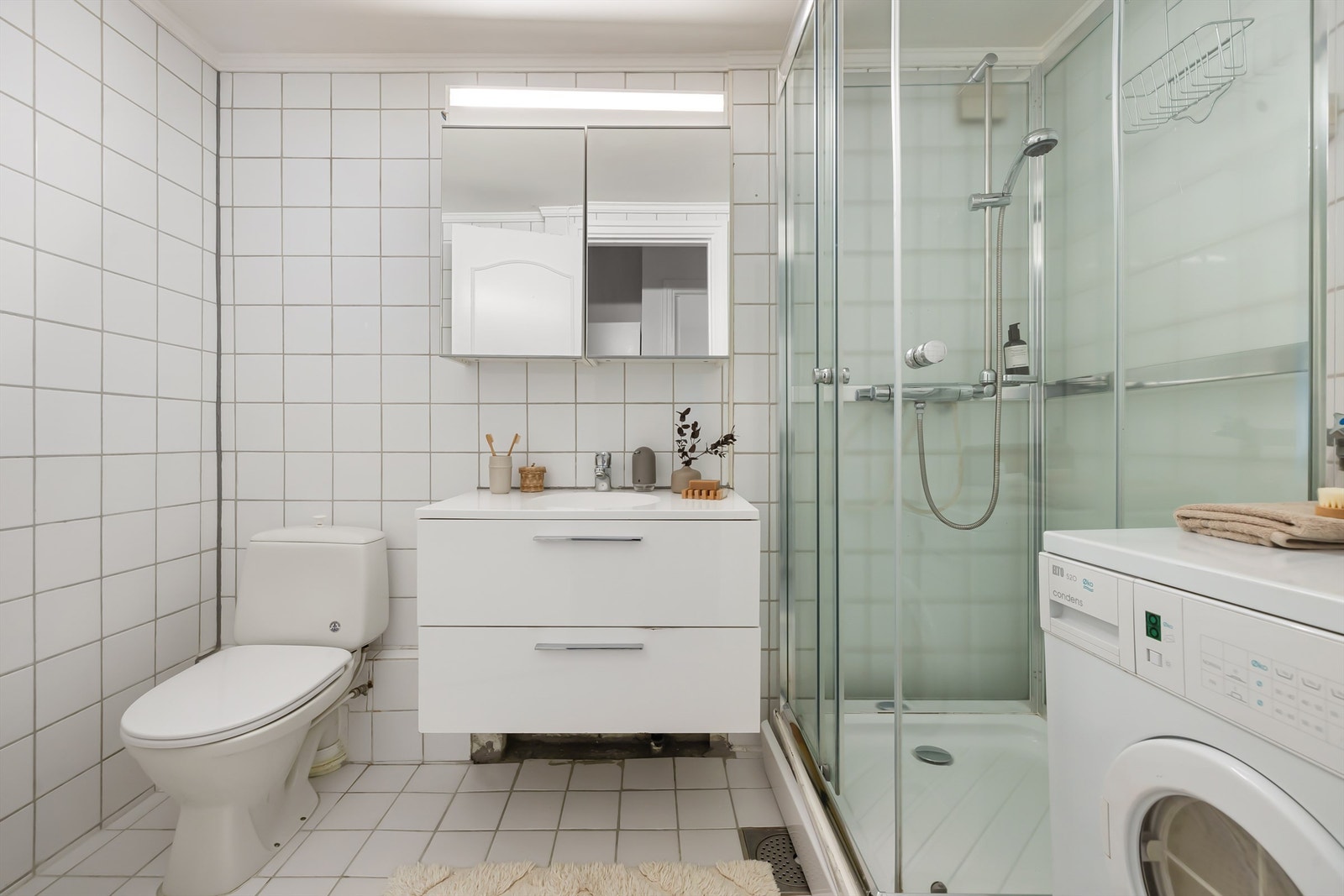 Ovenpåliggende servant med ett-greps armatur. Vegghengt speilskap med overbelysning. Galleribilde