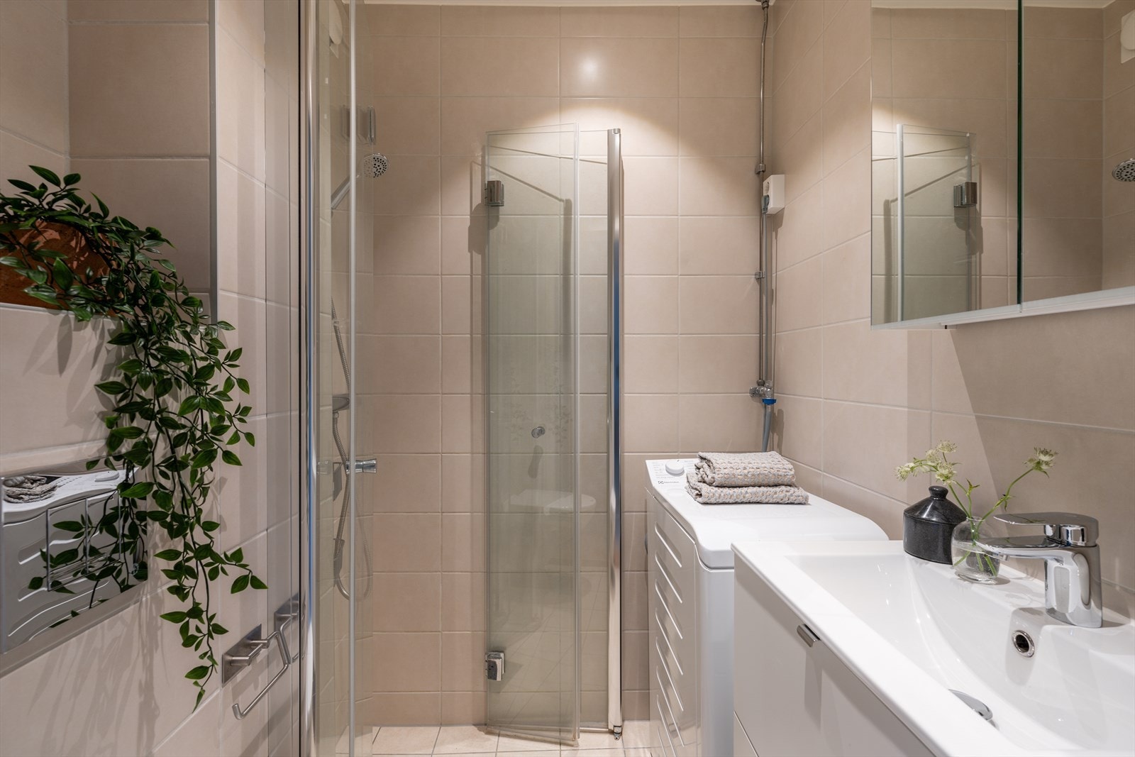 Badet er innredet med vegghengt klosett, en praktisk servant nedfelt i innredning, speilskap med belysning og et dusjhjørne med svingbare glassdører. Galleribilde