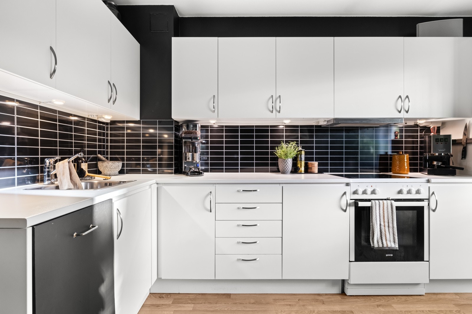 Innredningen har hvite, glatte fronter og benkeplate av laminat med stor oppvaskkum i rustfritt stål Galleribilde