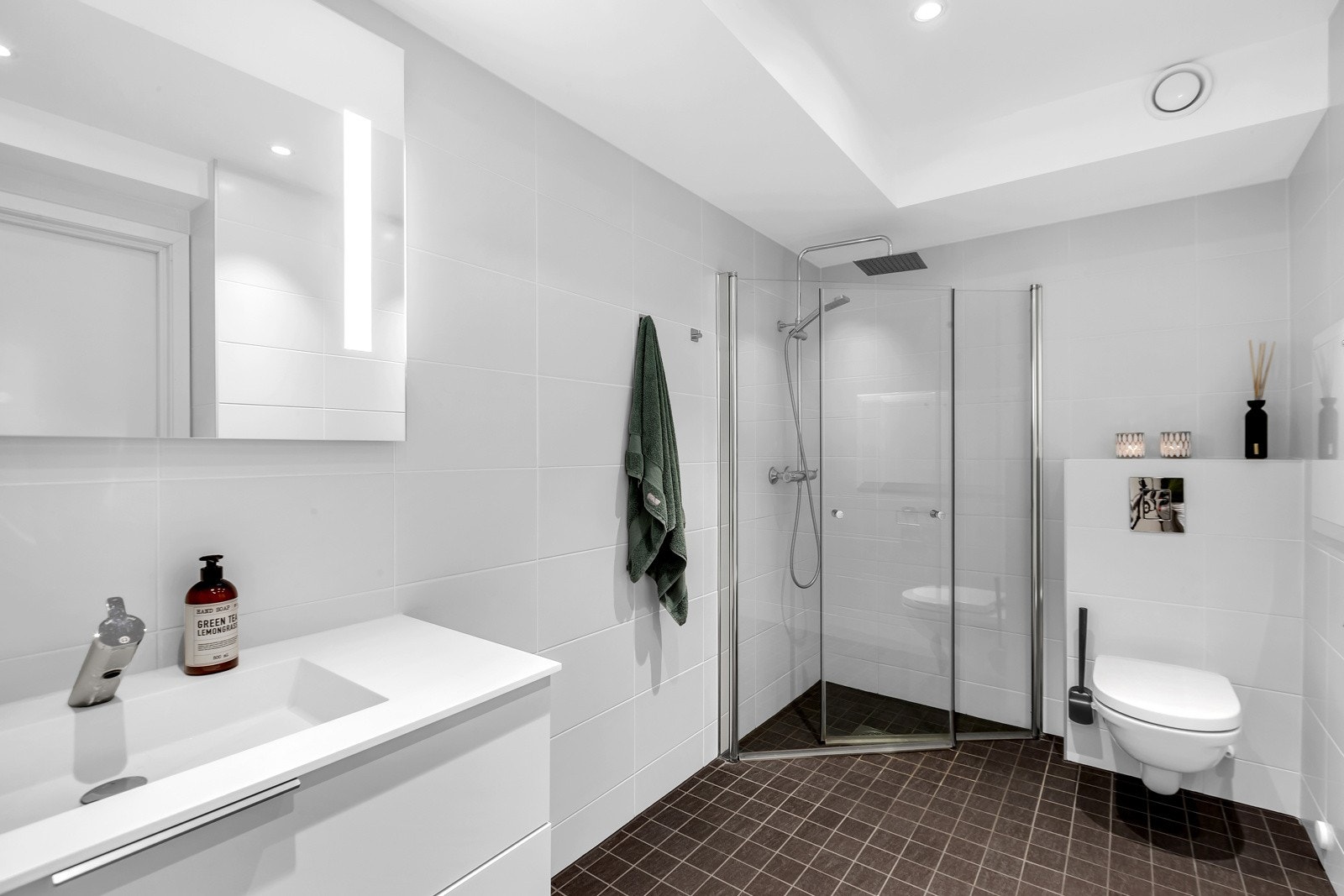 Badet er innredet med servant med ett-greps armatur, speil med belysning og dobbel stikkontakt på vegg, vegghengt toalett, dusjhjørne med ett-greps armatur med dusjhode samt hånddusj. Galleribilde