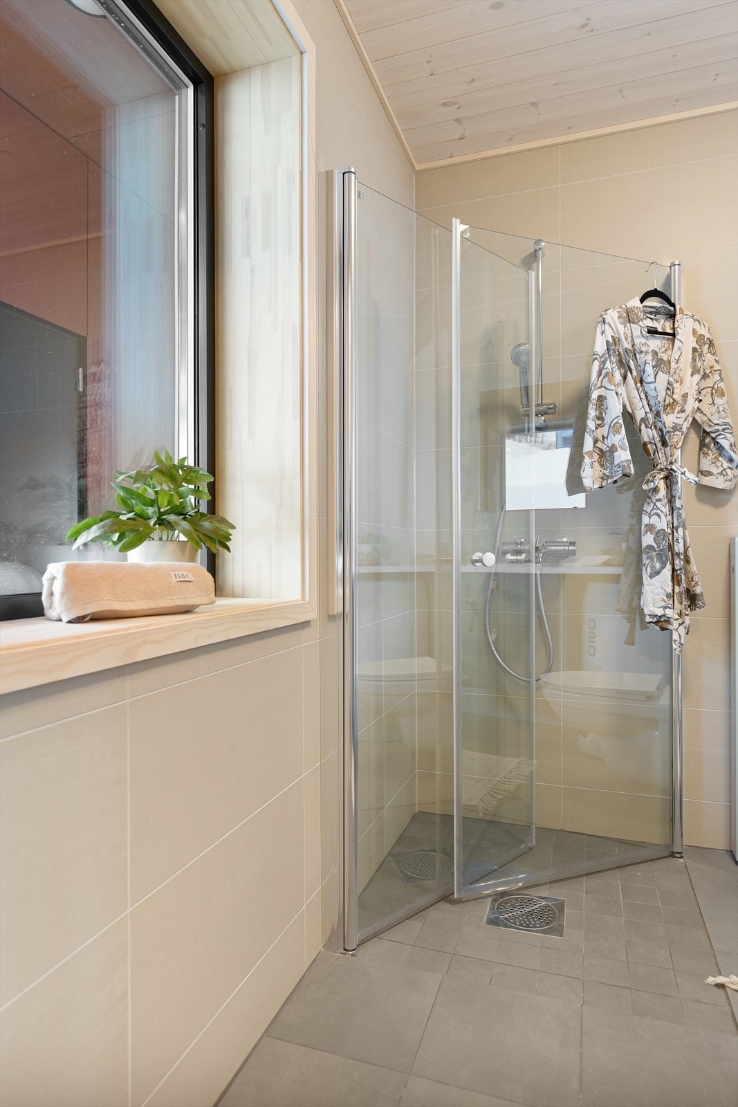 Servantmøbelet har heldekkende hvit servantplate og to vegghengte skuffer under. Dusjsonen er nedsenket med innfellbare dusjvegger som gir mer plass. Galleribilde