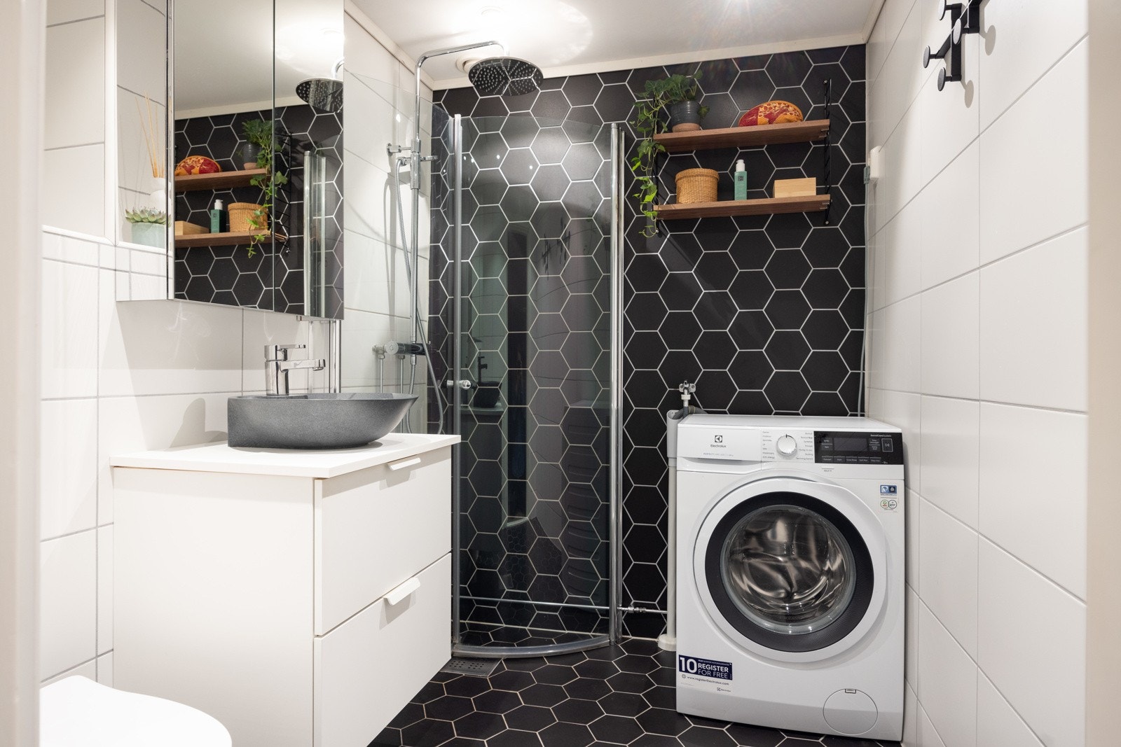 Fint, flislagt baderom som består av servant over innredning, speilskap på vegg, dusjhjørne og vegghengt toalett. Galleribilde