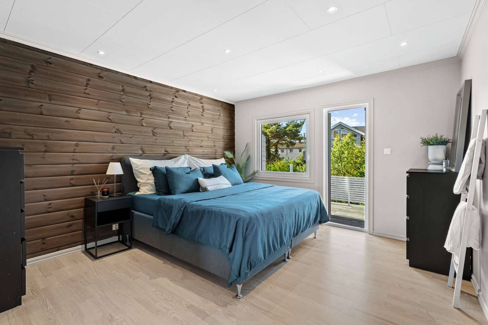 Hovedsoverommet har lyst laminatgulv, downlights i taket og glatte, lyse veggflater, som brytes opp av en fondvegg i mørkbeiset panel. Galleribilde